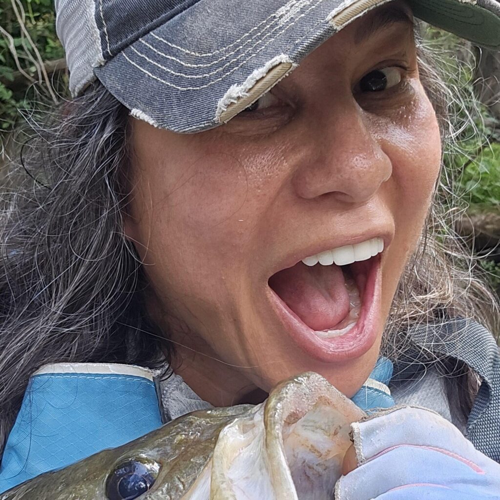 Mandie making a funny face while holding up a bass, kayak fishing